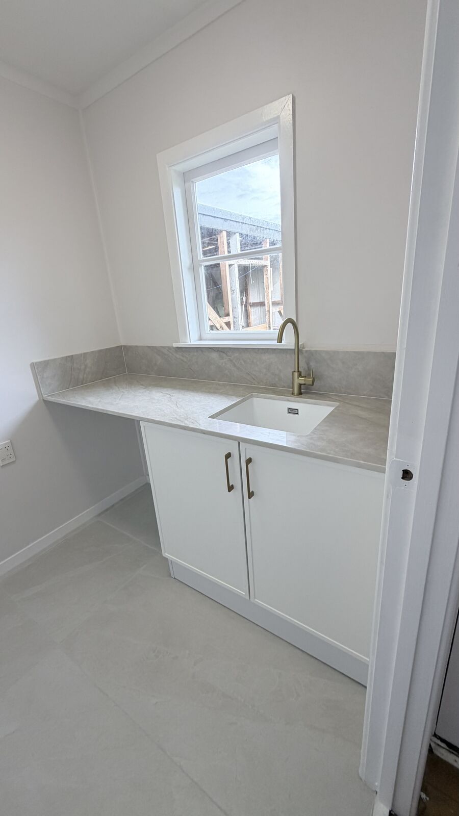Laundry renovation with stone benchtop and brushed brass tapware, Auckland